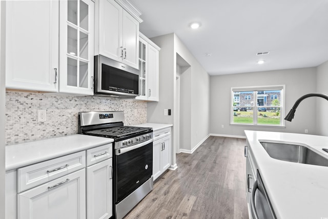 kitchen featuring tasteful backsplash, stainless steel appliances, white cabinetry, sink, and light hardwood / wood-style flooring