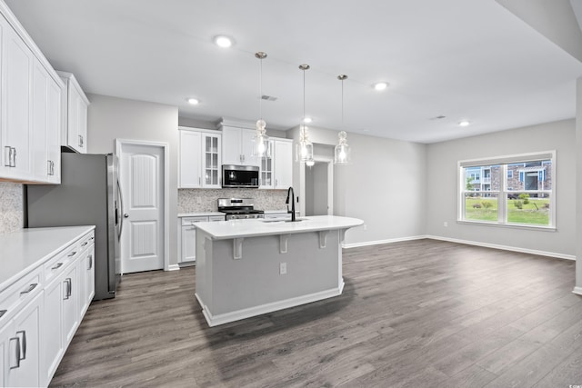 kitchen with white cabinetry, appliances with stainless steel finishes, hanging light fixtures, an island with sink, and dark wood-type flooring