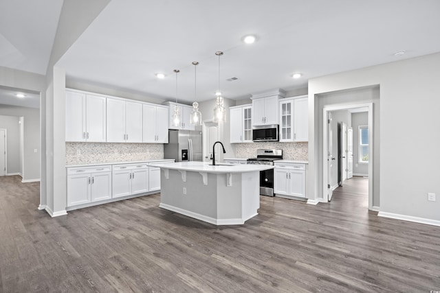 kitchen with pendant lighting, appliances with stainless steel finishes, an island with sink, and white cabinets