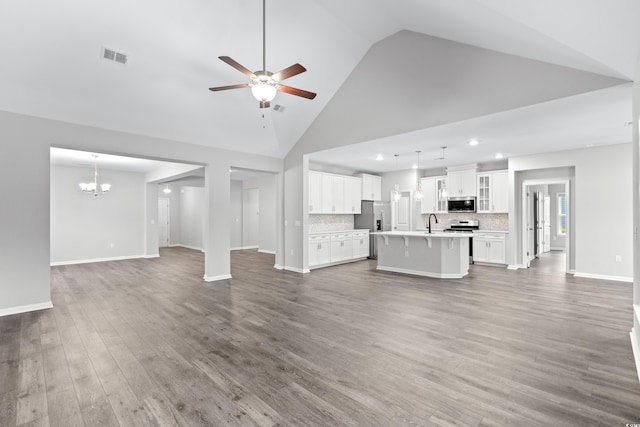 unfurnished living room featuring dark hardwood / wood-style flooring, high vaulted ceiling, sink, and ceiling fan with notable chandelier