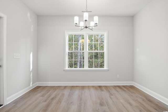 spare room featuring a notable chandelier and light wood-type flooring