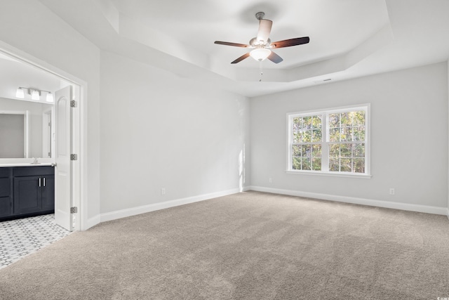 carpeted empty room with sink, a tray ceiling, and ceiling fan