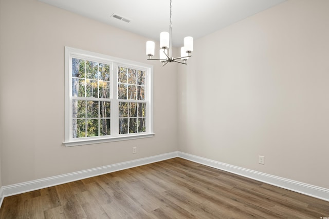 spare room with hardwood / wood-style flooring, plenty of natural light, and a chandelier