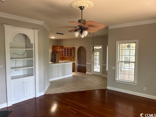 unfurnished living room with ceiling fan, crown molding, and dark wood-type flooring