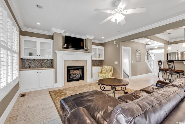 living room featuring a high end fireplace, ceiling fan, and crown molding