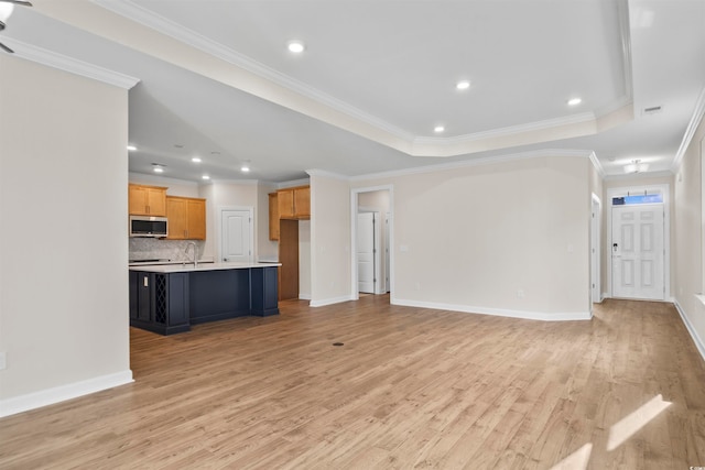 unfurnished living room with sink, a raised ceiling, light hardwood / wood-style floors, and crown molding