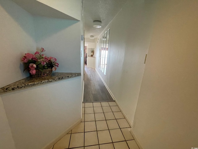 hallway featuring a textured ceiling, light tile patterned flooring, and baseboards