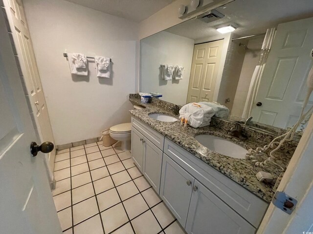 bathroom with toilet, tile patterned floors, and double sink vanity