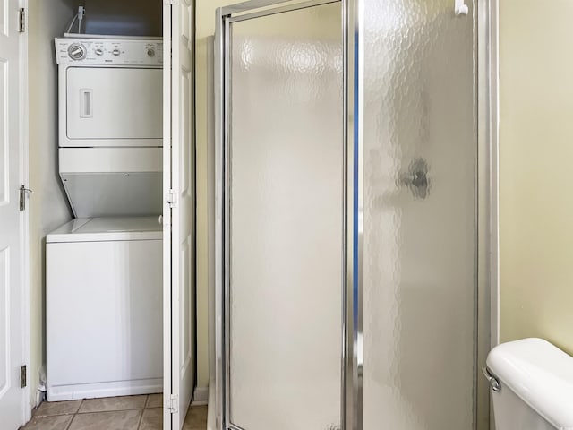 bathroom with tile floors, stacked washer and clothes dryer, toilet, and a shower with shower door