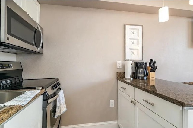 kitchen with white cabinets, appliances with stainless steel finishes, dark stone counters, and pendant lighting