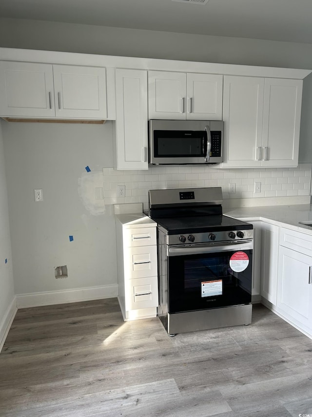 kitchen featuring tasteful backsplash, light hardwood / wood-style flooring, white cabinets, and appliances with stainless steel finishes