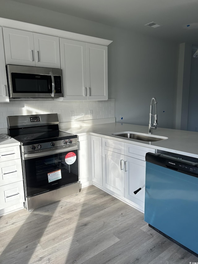 kitchen with white cabinets, sink, light hardwood / wood-style flooring, decorative backsplash, and stainless steel appliances