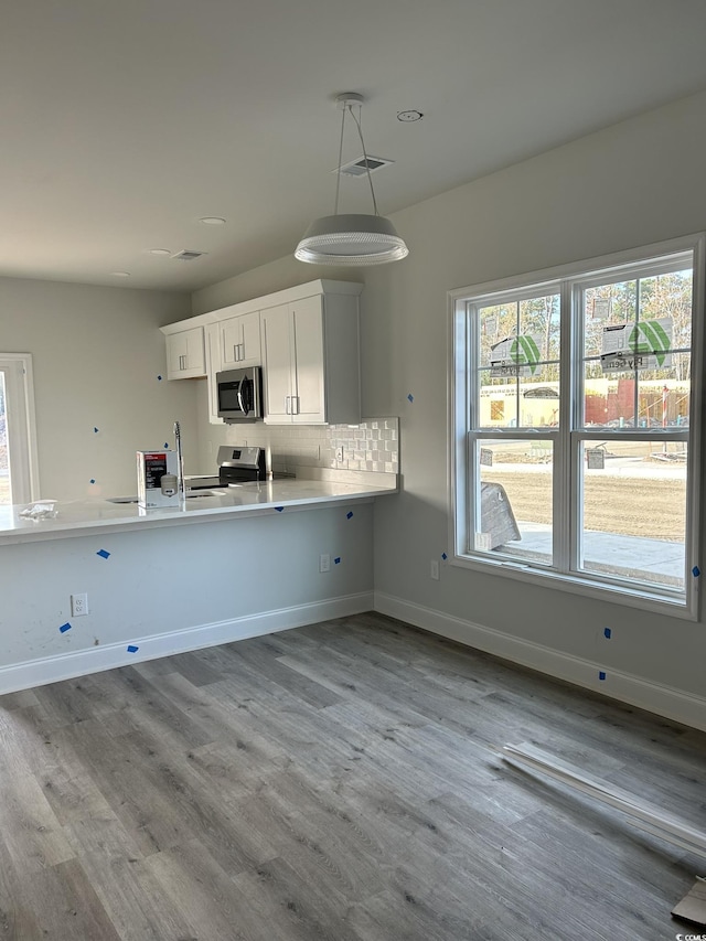 kitchen featuring white cabinets, light hardwood / wood-style flooring, appliances with stainless steel finishes, decorative light fixtures, and kitchen peninsula