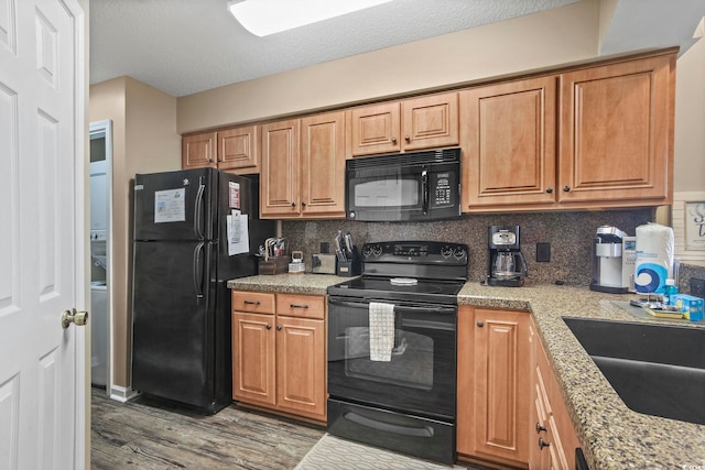 kitchen with tasteful backsplash, black appliances, dark hardwood / wood-style flooring, light stone counters, and sink