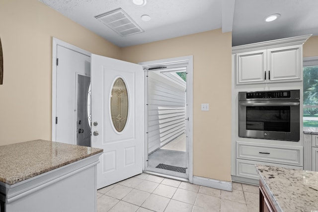 kitchen featuring white cabinets, oven, light stone countertops, a textured ceiling, and light tile patterned floors