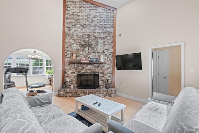 living room with light hardwood / wood-style flooring, high vaulted ceiling, a notable chandelier, and a brick fireplace