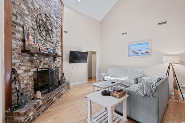 living room with light hardwood / wood-style floors, high vaulted ceiling, and a brick fireplace