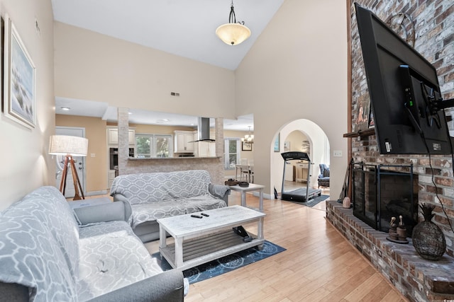 living room featuring an inviting chandelier, a fireplace, high vaulted ceiling, and light hardwood / wood-style flooring