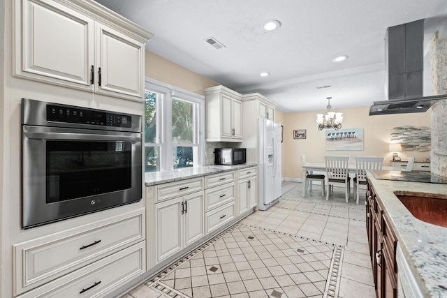 kitchen featuring white fridge with ice dispenser, an inviting chandelier, light stone counters, range hood, and oven