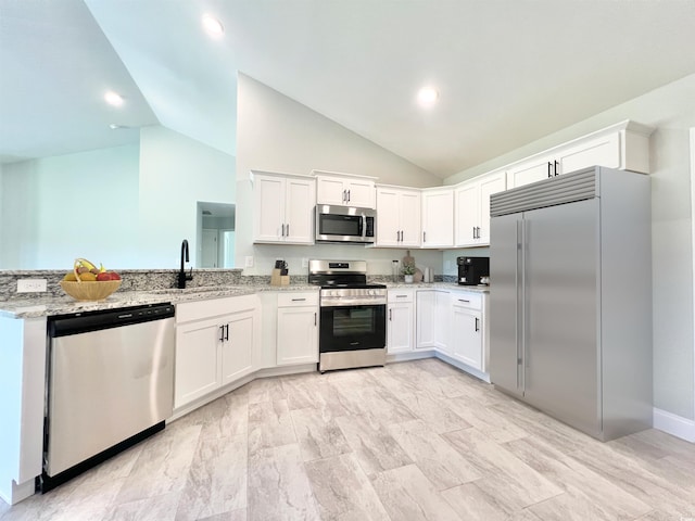 kitchen with kitchen peninsula, sink, light stone countertops, white cabinets, and appliances with stainless steel finishes