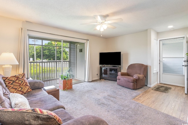 living room with a textured ceiling, ceiling fan, and light wood-type flooring