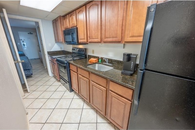 kitchen with a paneled ceiling, dark stone counters, black appliances, sink, and light tile patterned floors