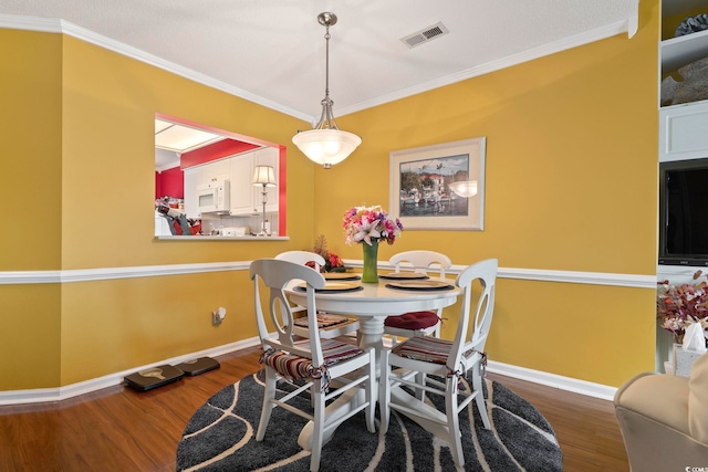 dining room with crown molding, baseboards, visible vents, and wood finished floors