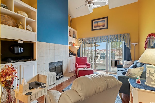 living room with a tiled fireplace, built in shelves, light wood-type flooring, and ceiling fan