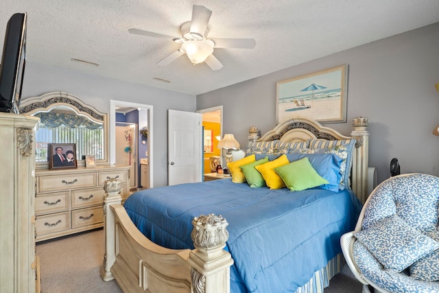 bedroom with a ceiling fan, a textured ceiling, visible vents, light colored carpet, and ensuite bath