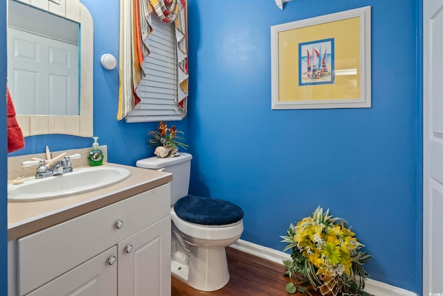 half bathroom with toilet, baseboards, wood finished floors, and vanity