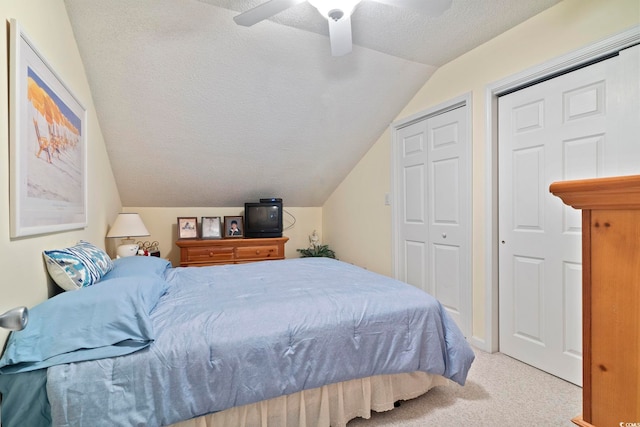 carpeted bedroom with ceiling fan, multiple closets, a textured ceiling, and vaulted ceiling