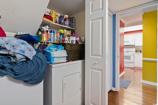 clothes washing area featuring laundry area, light wood-style floors, baseboards, washer / clothes dryer, and a textured ceiling