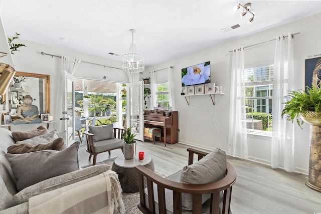 living room with light wood-type flooring, french doors, and an inviting chandelier