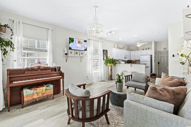 living room featuring ceiling fan with notable chandelier and light wood-type flooring