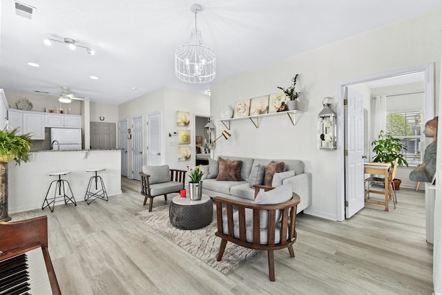 living room with ceiling fan with notable chandelier and light wood-type flooring