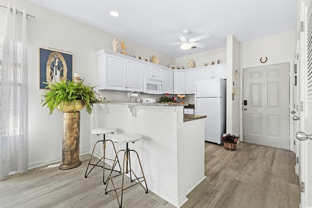 kitchen featuring white cabinetry, kitchen peninsula, light hardwood / wood-style floors, white appliances, and a breakfast bar area