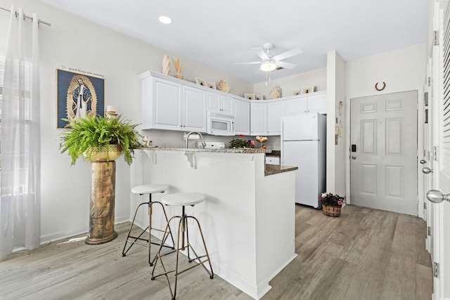242 Sun Colony Blvd Unit 101, Longs, SC 29568 - kitchen featuring white appliances, a peninsula, light wood-style flooring, a kitchen bar, and a ceiling fan