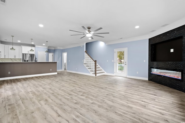 unfurnished living room with ceiling fan, a large fireplace, light hardwood / wood-style flooring, and ornamental molding