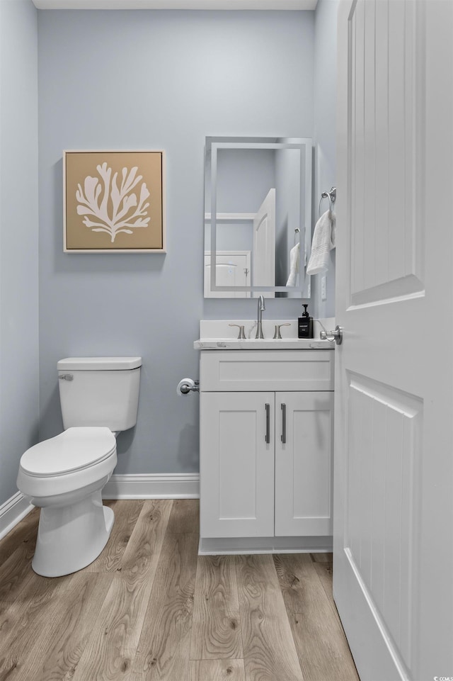 half bath with baseboards, toilet, vanity, and wood finished floors