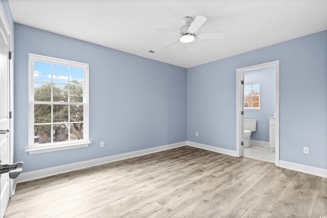 unfurnished bedroom featuring ensuite bathroom, light hardwood / wood-style flooring, multiple windows, and ceiling fan