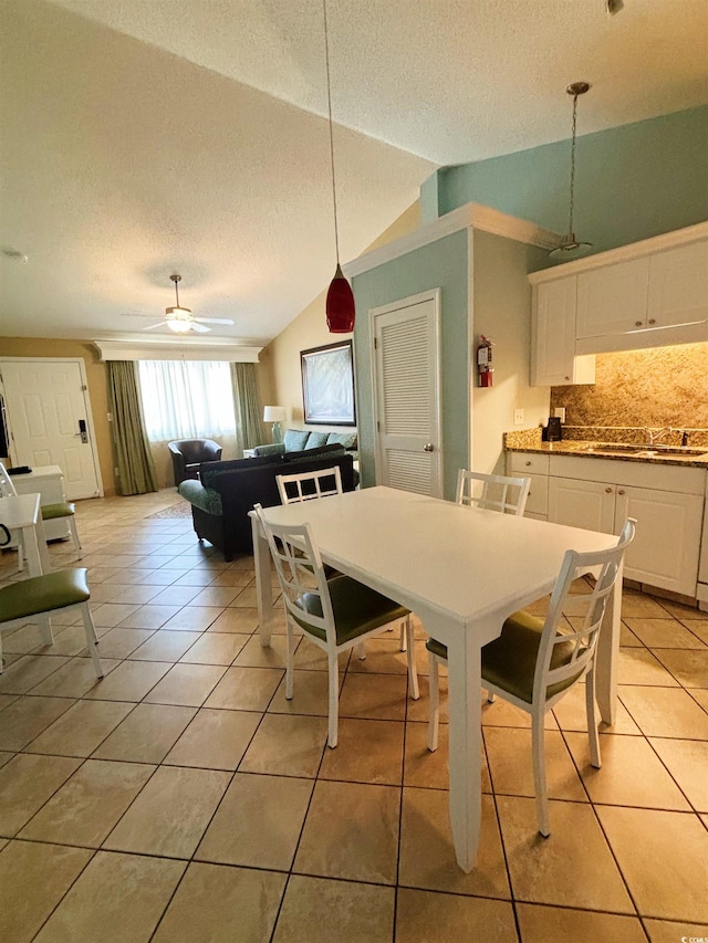 dining area with ceiling fan, vaulted ceiling, a textured ceiling, and light tile floors