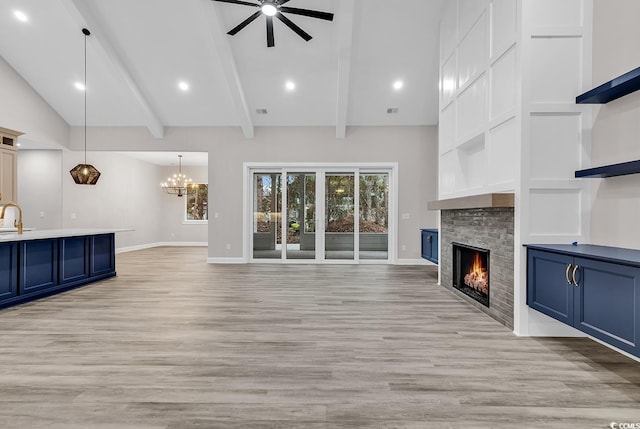 unfurnished living room featuring ceiling fan with notable chandelier, sink, high vaulted ceiling, light hardwood / wood-style flooring, and a stone fireplace