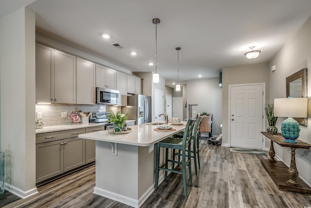 kitchen with backsplash, gray cabinetry, hardwood / wood-style flooring, an island with sink, and appliances with stainless steel finishes