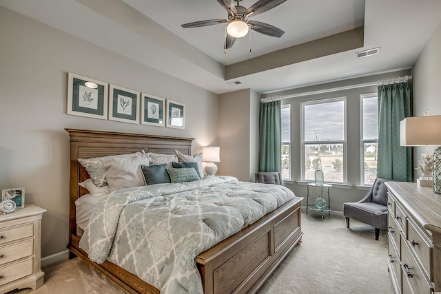 bedroom featuring ceiling fan, a tray ceiling, and light carpet