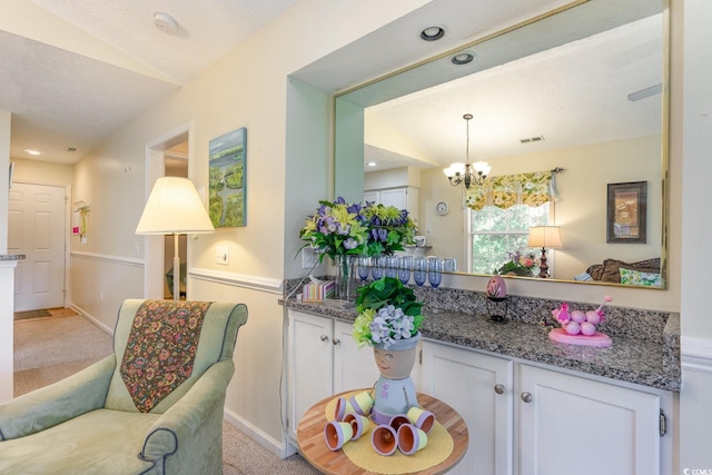 kitchen featuring white cabinetry, a chandelier, stone counters, and light colored carpet