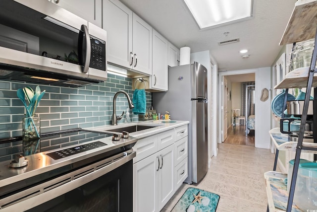 kitchen featuring stainless steel appliances, light tile flooring, backsplash, sink, and white cabinetry