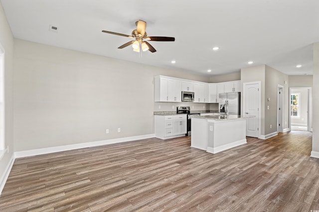 kitchen featuring stainless steel appliances, white cabinetry, baseboards, light wood finished floors, and an island with sink