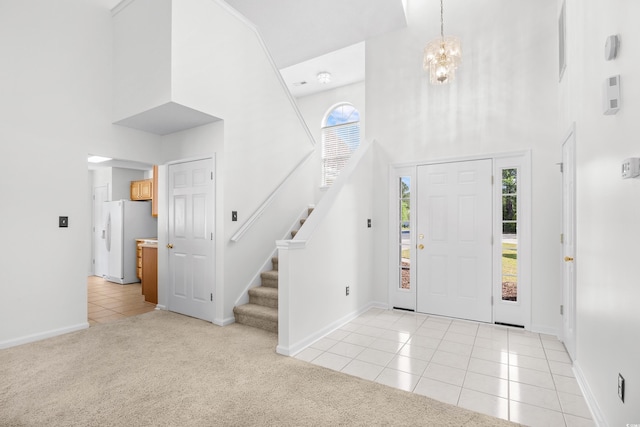 foyer entrance with a high ceiling, light tile patterned floors, a chandelier, baseboards, and light carpet
