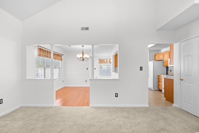 unfurnished living room with a chandelier, light carpet, healthy amount of natural light, and high vaulted ceiling