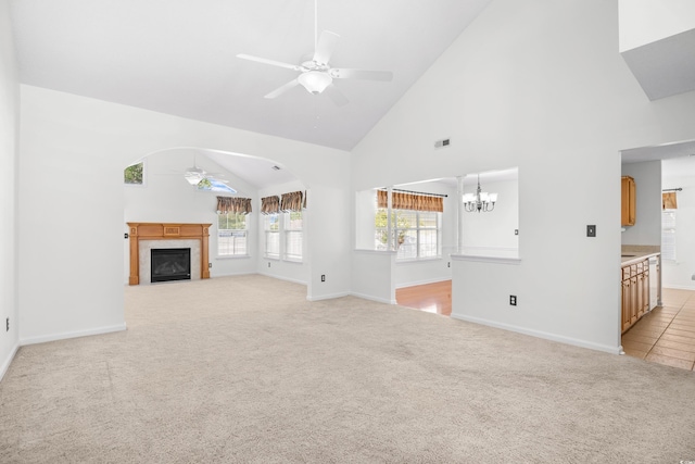 unfurnished living room with a ceiling fan, high vaulted ceiling, a tiled fireplace, light carpet, and baseboards
